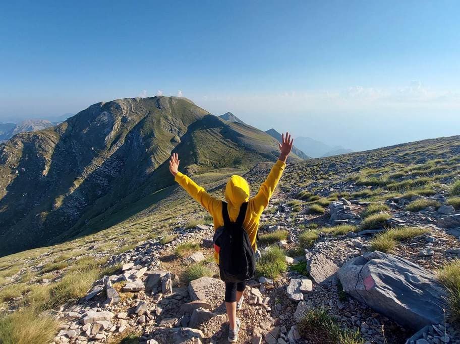 Guided hiker with arms raised at the stone chapel on the 2407m summit of Mount Taygetos, Peloponnese