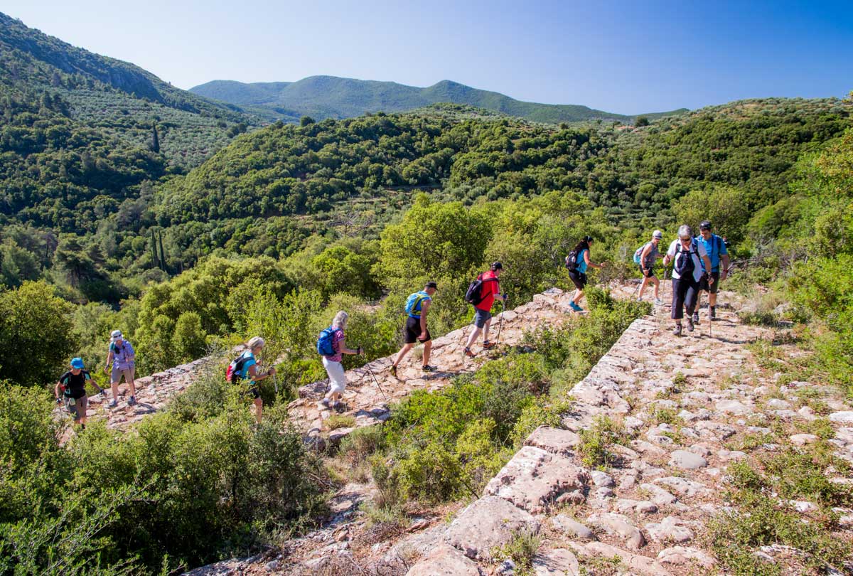 Guided hikers descending the historic stone-built Biliovo Trail zig-zags in Mani with views of the Messinian Gulf