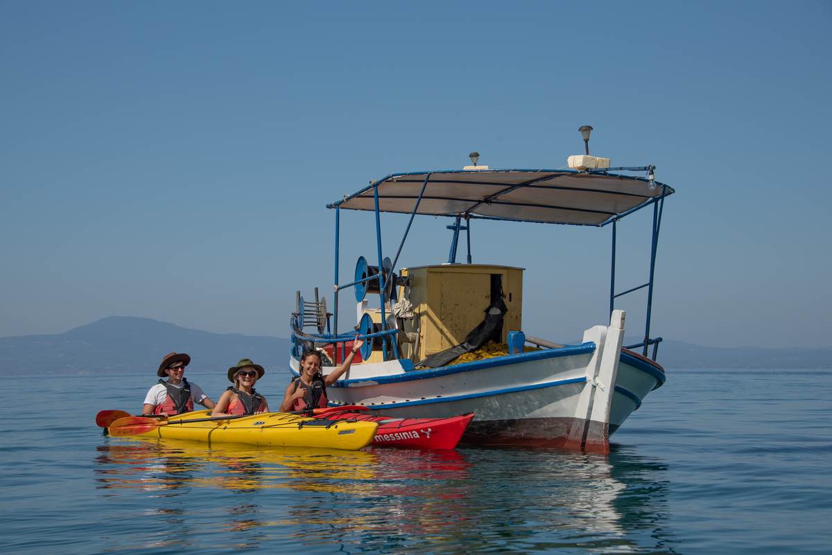 Paddlers waving next to a traditional wooden Greek fishing boat