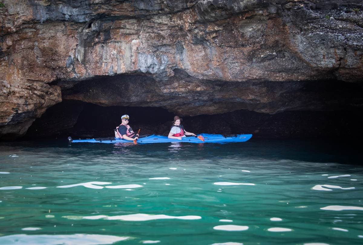 Two people exploring the entrance of a dark coastal sea cave