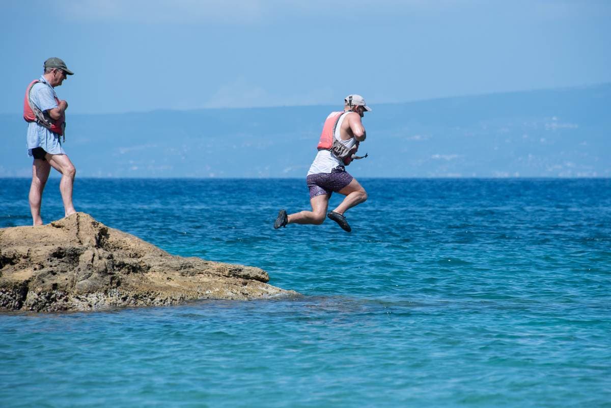Man jumping into the deep blue sea from a rocky outcrop