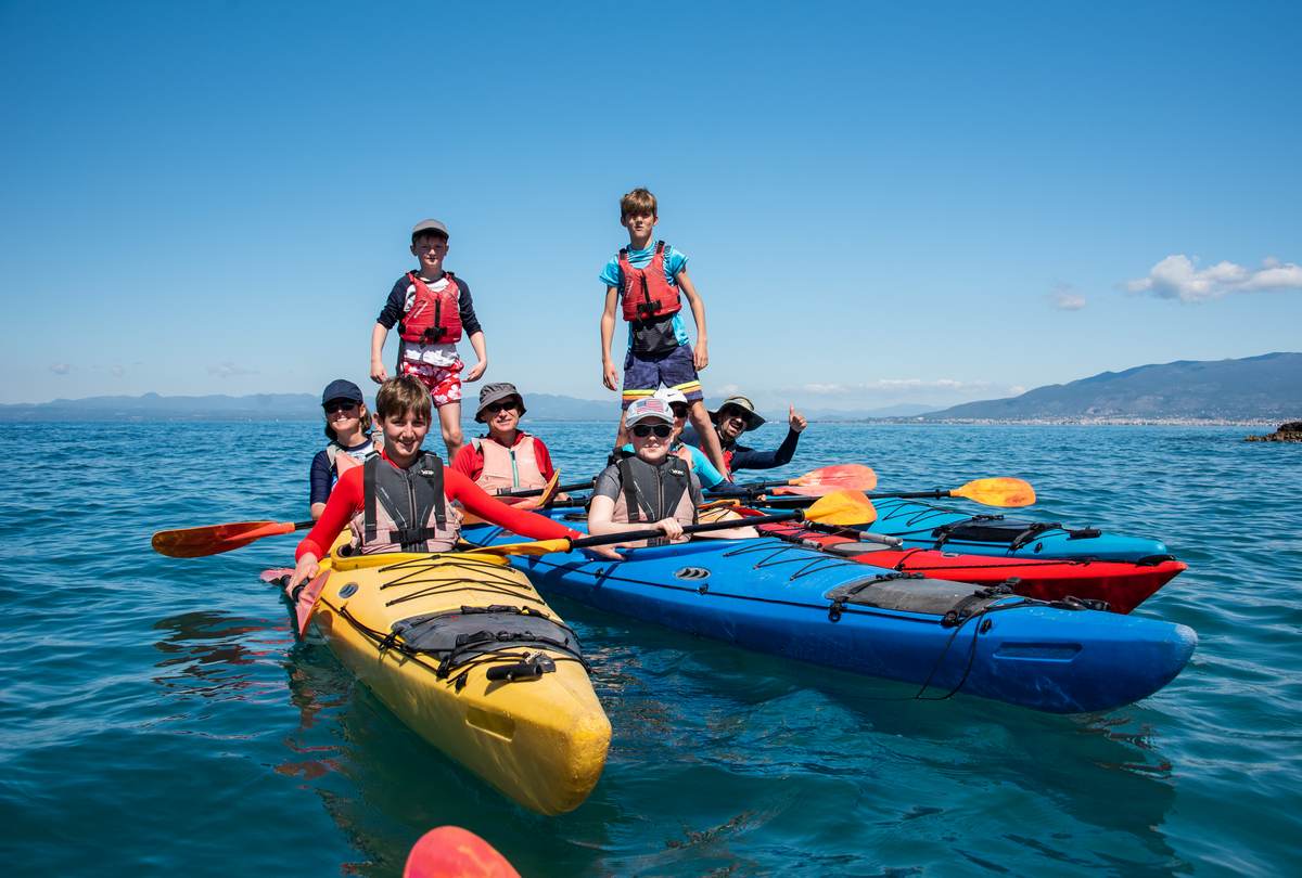 Family group posing on colorful kayaks in the middle of a blue bay