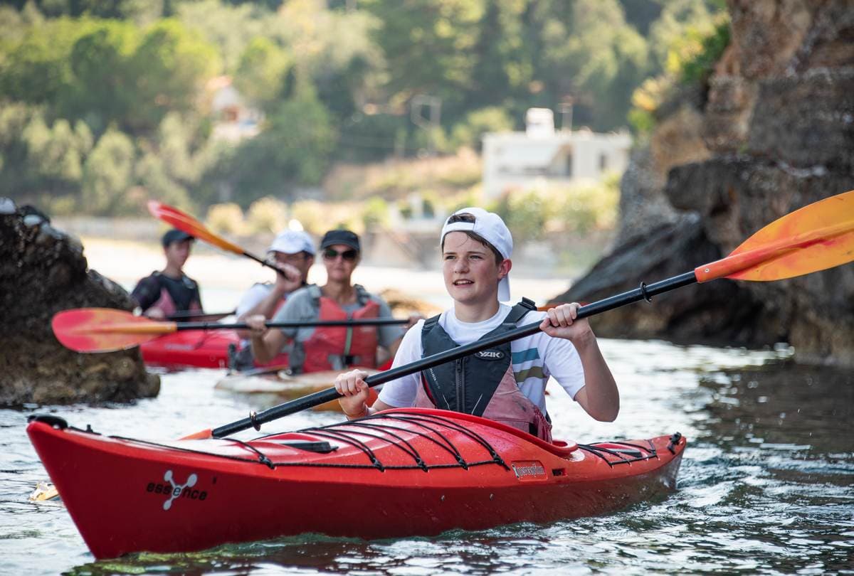 Young boy paddling a red kayak with focus and excitement