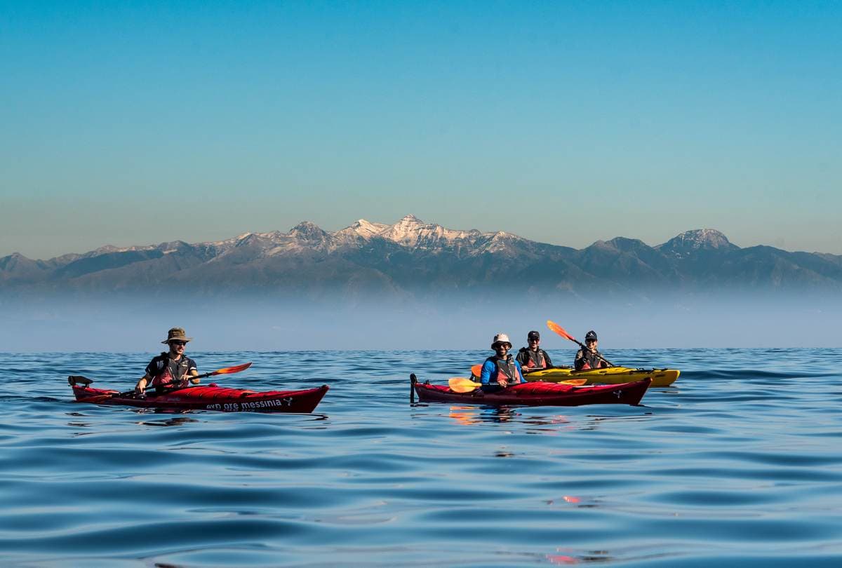 A group of travelers enjoying sea kayaking in the Peloponnese with a backdrop of snow-capped mountains.