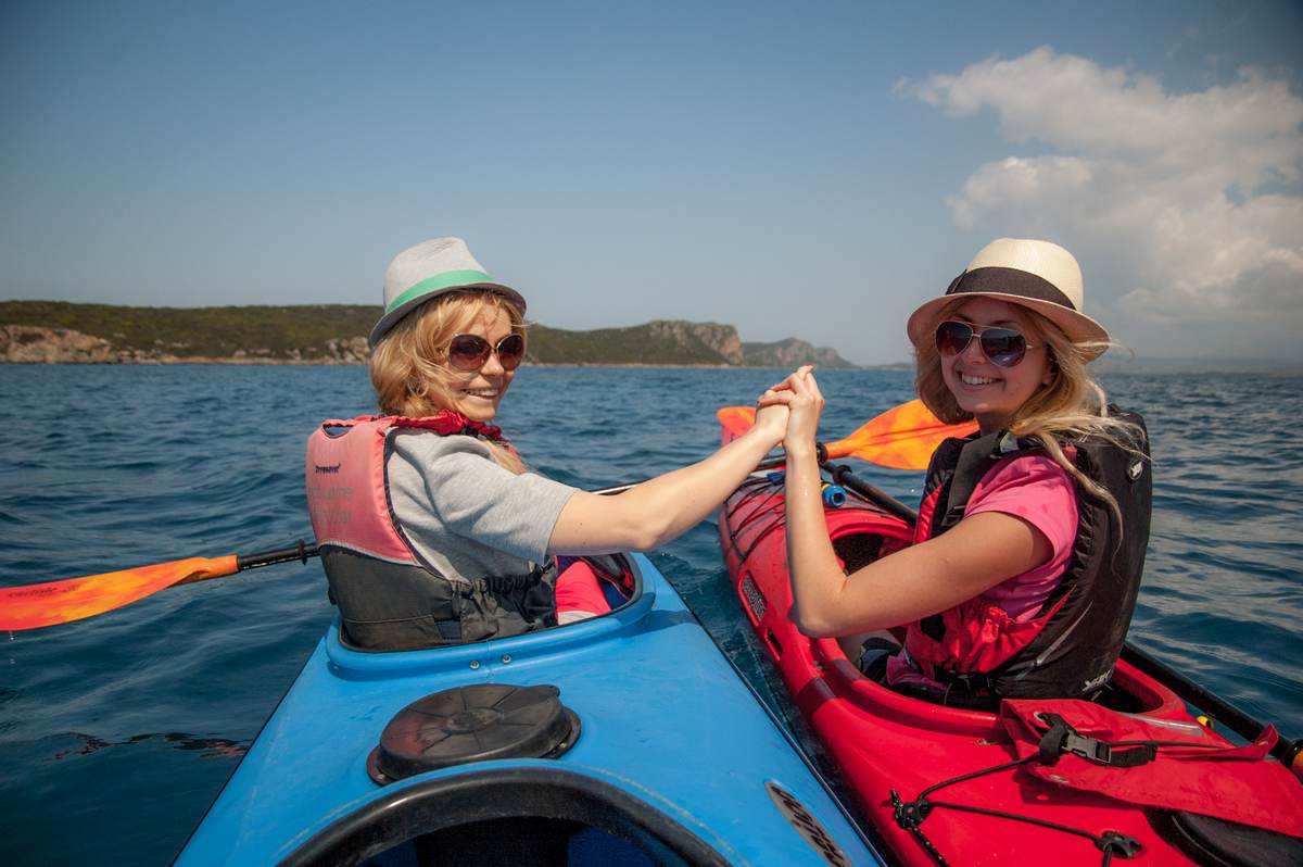 Two women in sun hats smiling while holding hands between their kayaks