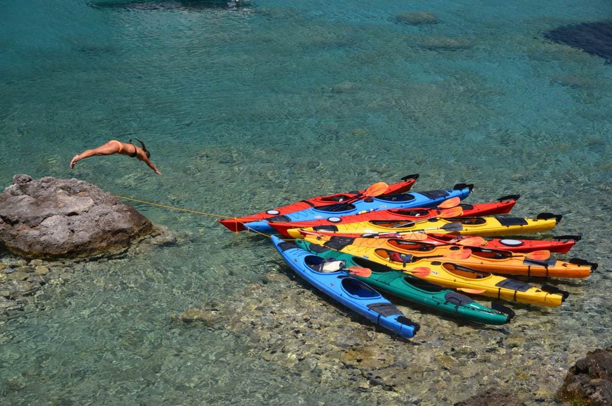 Travelers in kayaks forming a flower shape in shallow, transparent Mediterranean water.