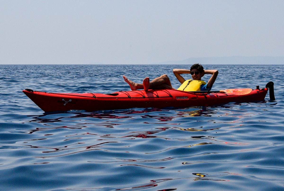 A traveler relaxing and lying back in a red kayak on the calm, open waters of the Messinian Gulf.