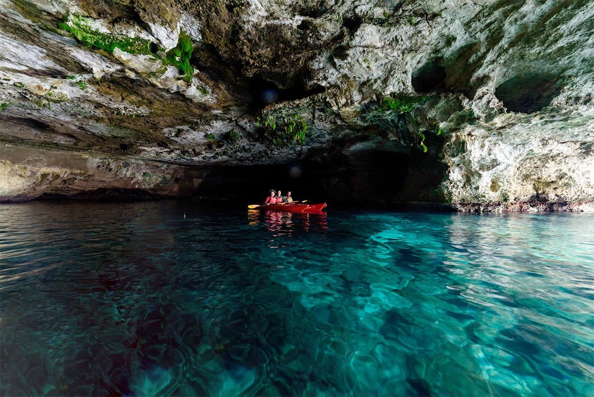 The interior of a large sea cave in Mani with turquoise water and light reflecting off the cave ceiling.