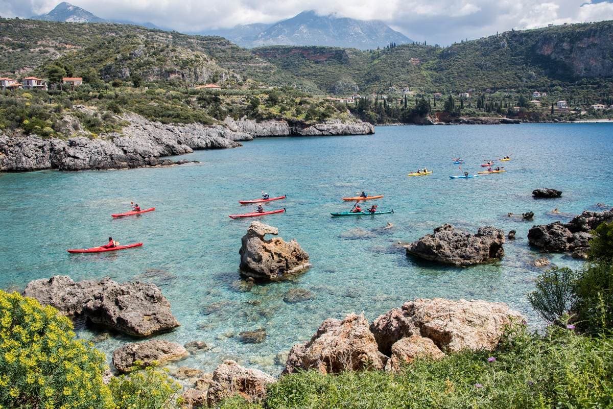 Group of travelers in colorful kayaks exploring a turquoise cove in the Peloponnese on a sea kayak Kardamyli tour.