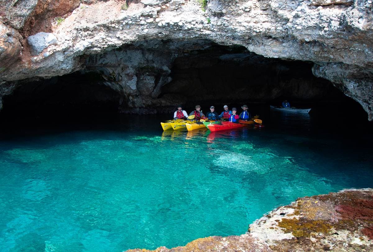 Group of kayakers gathered inside a spacious sea cave with vibrant turquoise water.