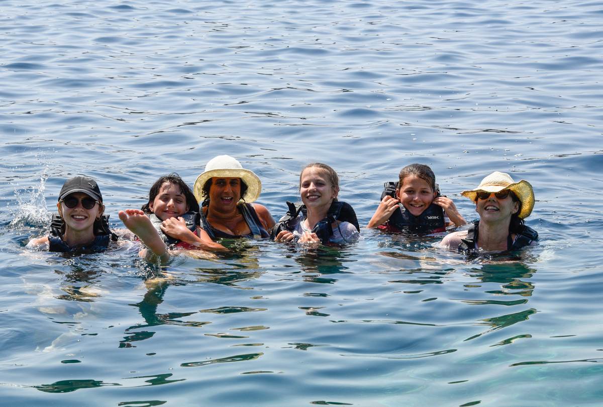 Group of six women wearing life jackets swimming and laughing in the open sea.