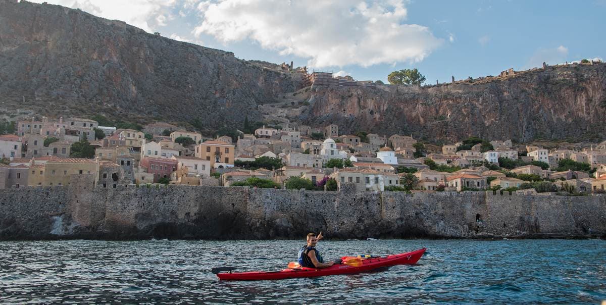 A traveler paddling a red kayak near the city walls while Sea Kayaking Monemvasia