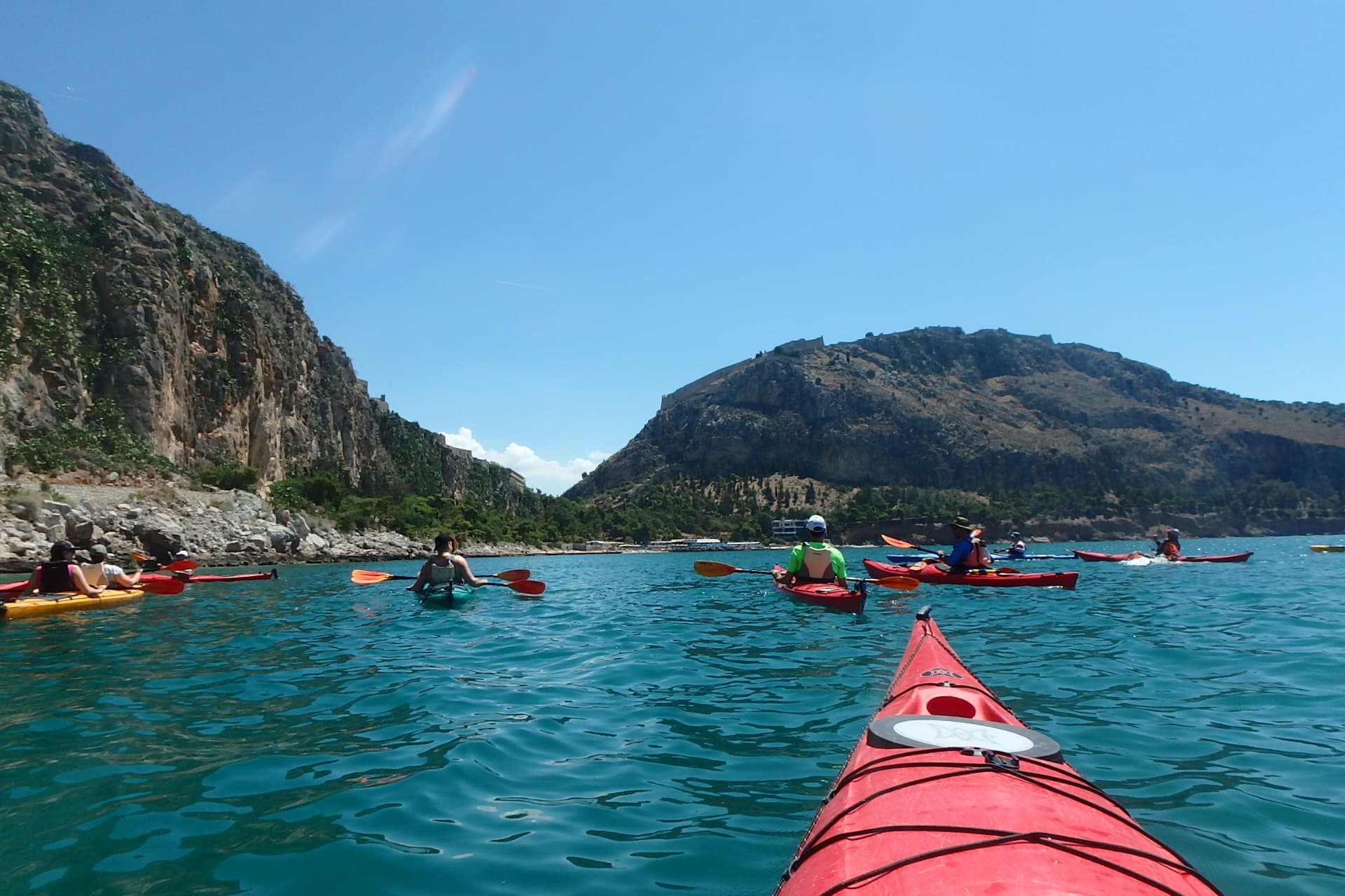 Group of colorful kayaks in the Argolic Gulf with Palamidi Castle seen while Sea Kayaking Nafplio