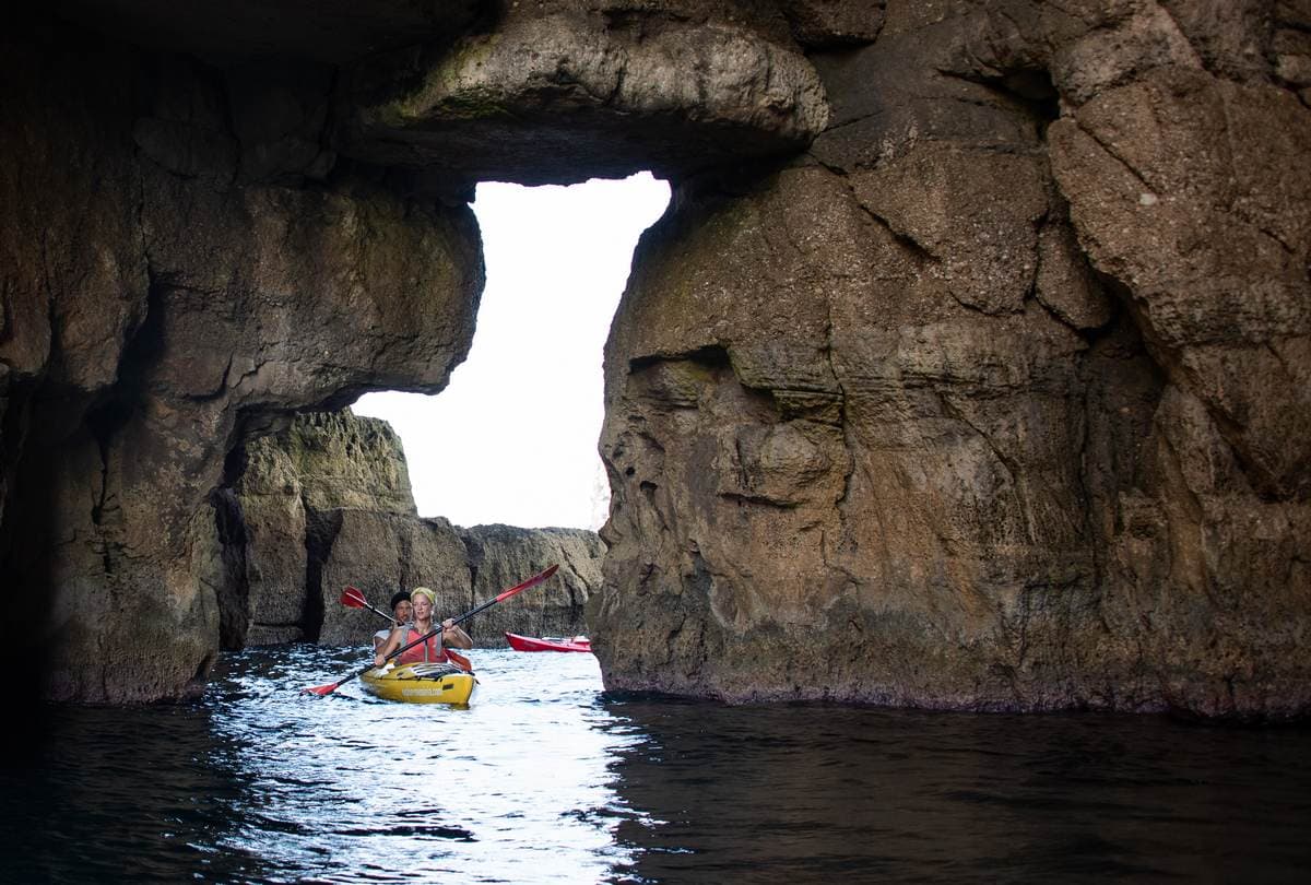 A yellow tandem kayak navigating through a narrow rock passage under a natural arch.