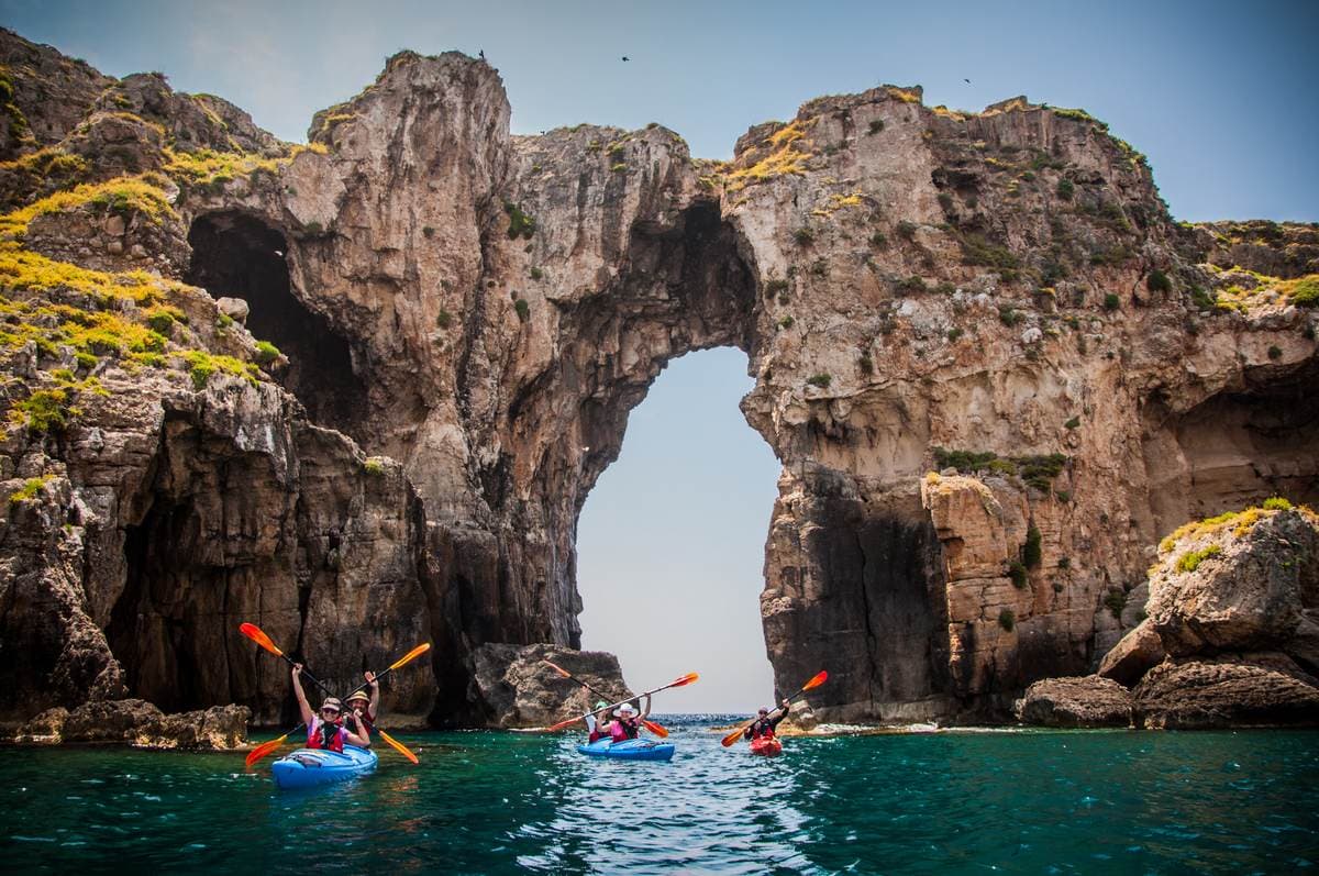 Three kayaks in a line in front of the massive natural stone arch of Tsihli Baba islet.