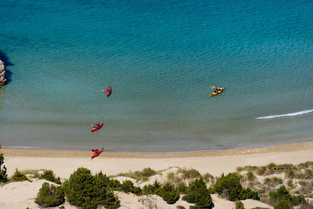 High-angle view of red and yellow kayaks in shallow turquoise water near a sandy beach.