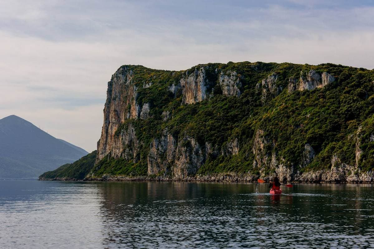 A kayaker dwarfed by the massive limestone cliffs of Sphacteria Island in Navarino Bay, Peloponnese.