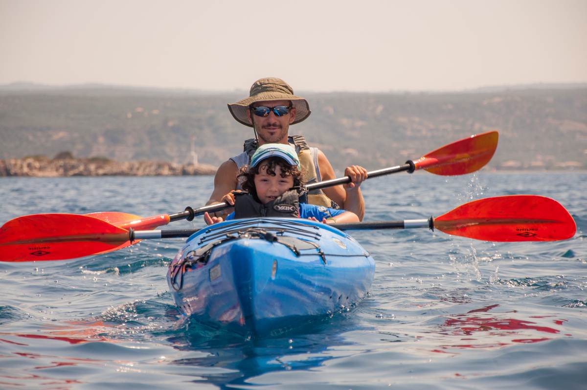 A guide and a young child in a blue tandem kayak enjoying a calm day on the water in Pylos, Greece.