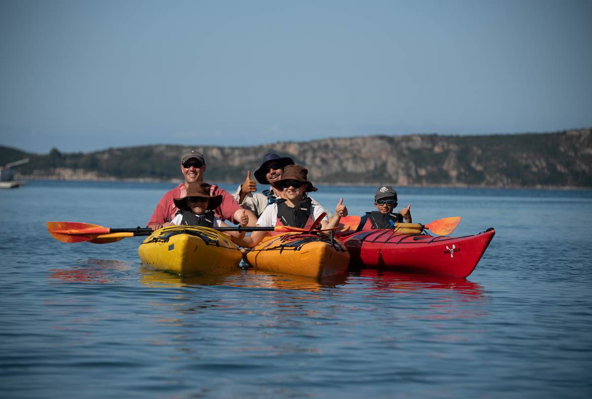 A group of travelers in kayaks giving thumbs up on a calm, sunny day in Navarino Bay, Greece.