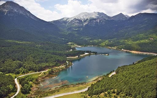 Lake Doxa's emerald water ringed by pine forest below mountain peaks