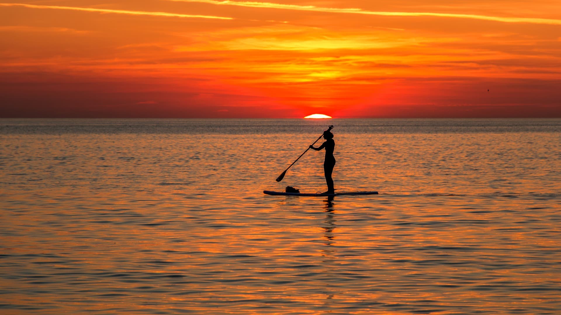 Stand-up paddleboarder silhouetted on calm sea at sunset off Messinia