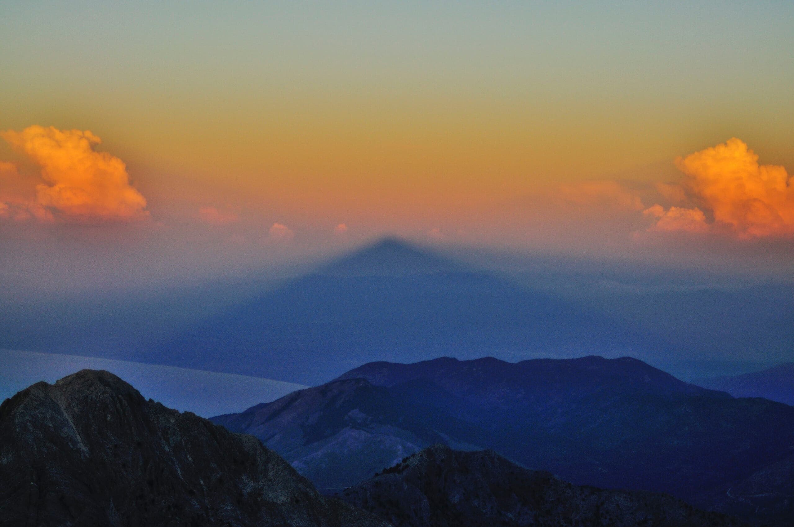 Triangular shadow of Taygetos peak cast over hazy mountains at sunset with orange clouds
