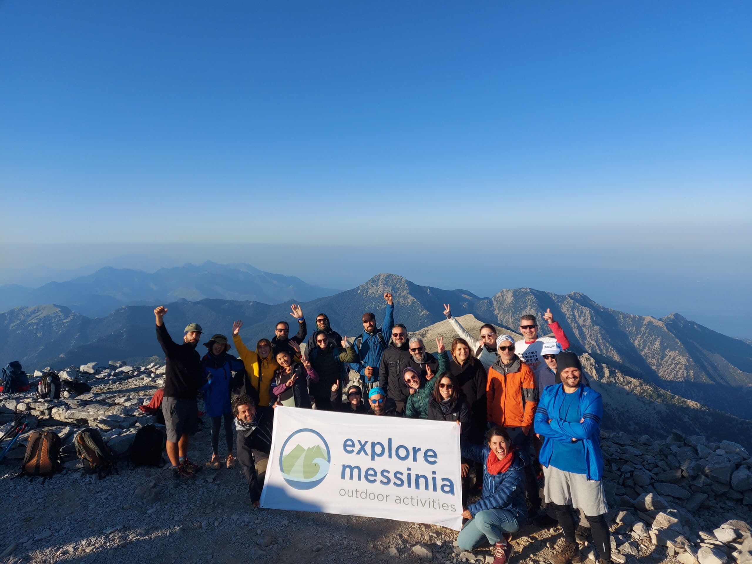 Hiking group with Explore Messinia banner on Taygetos summit above haze-filled valleys