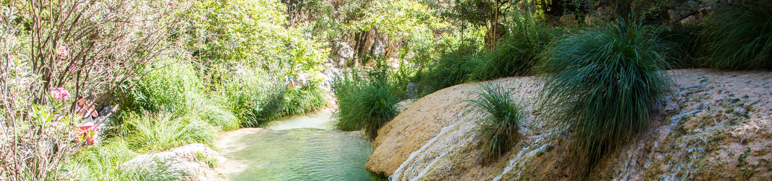 Panoramic view of the lush Polylimnio gorge with turquoise tiered waterfalls and natural pools in Messinia