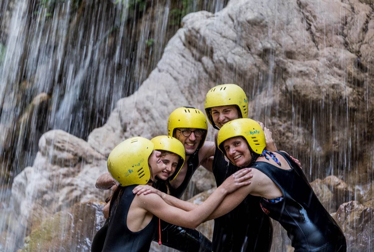 A happy family wearing safety helmets during a guided canyoning adventure in Greece.