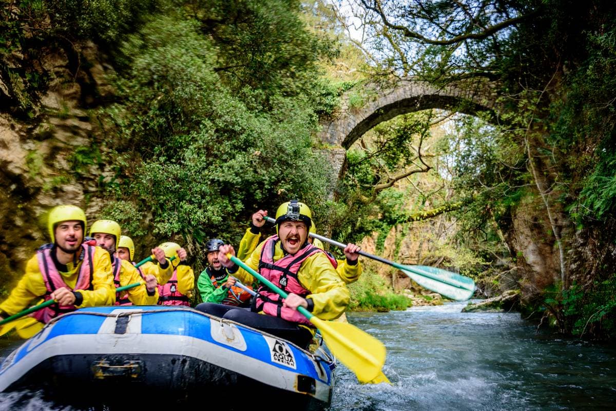 A guided group during one of our professional rafting tours in Greece paddling under an ancient stone bridge.