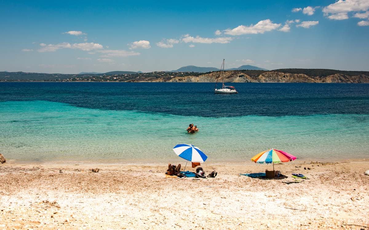 Scenic view of a turquoise beach with colorful umbrellas and an anchored sailboat