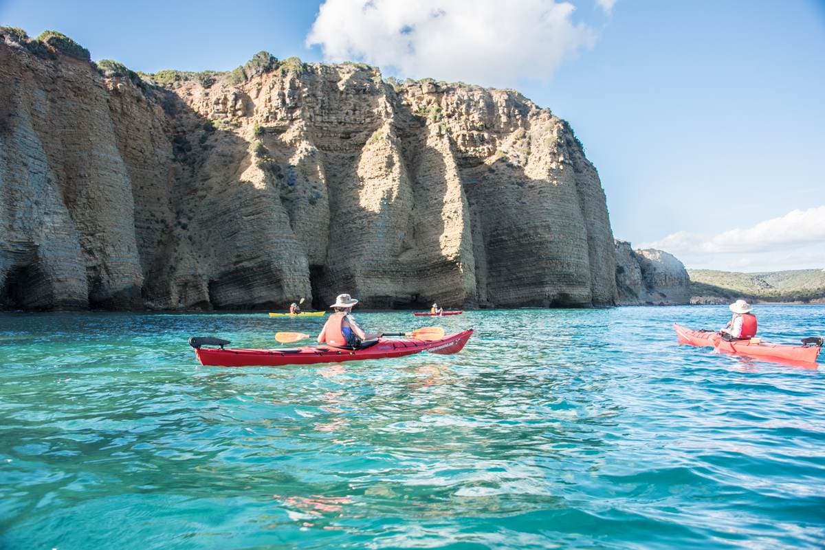 Three sea kayakers exploring the base of high coastal cliffs on a calm day