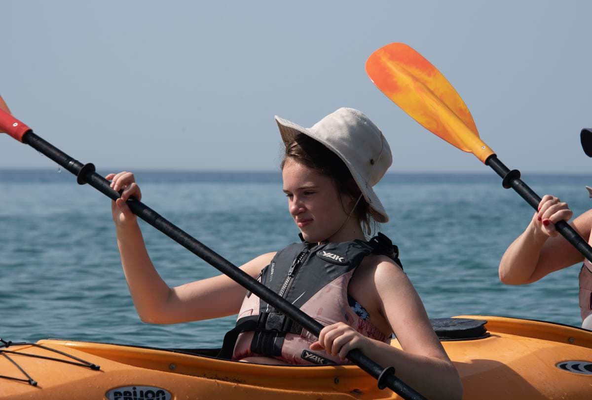 Focused young girl in a sun hat paddling her yellow sea kayak with care