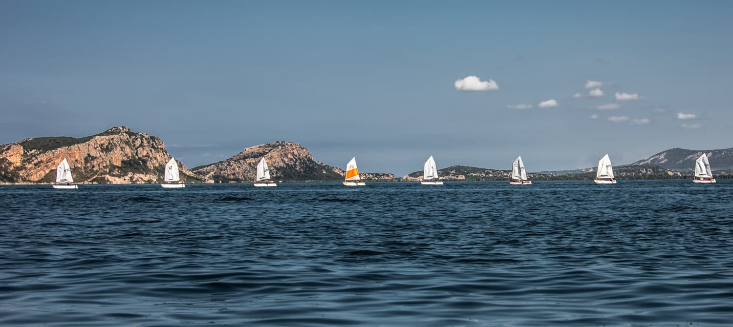 Small sailing dinghies racing across Navarino Bay below rocky headlands during the 2016 challenge