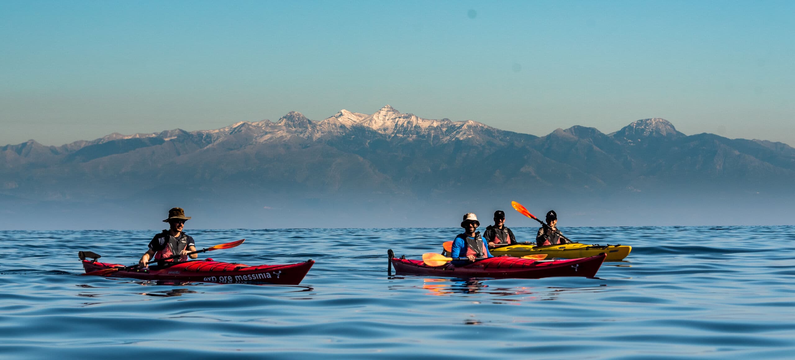 A group of explorers on an Adventure Tour in Peloponnese navigating clear turquoise waters in sea kayaks.