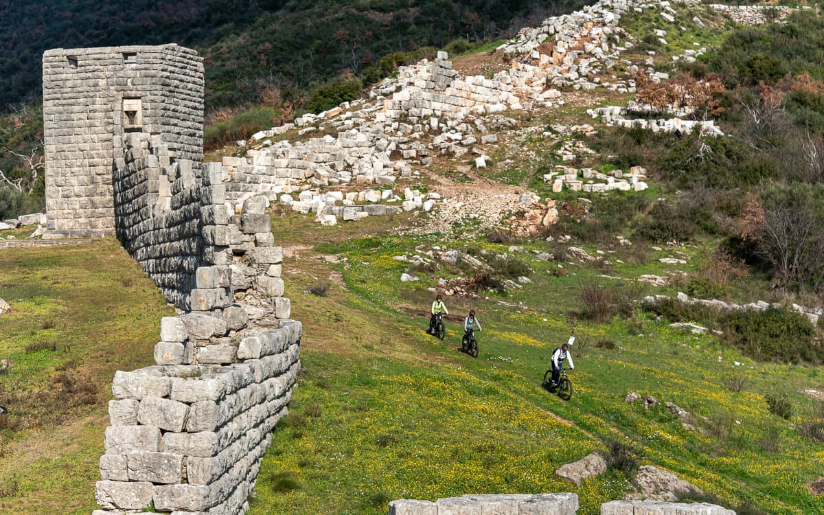 Cyclists riding next to massive stone ruins during an Ancient Messene E-Bike Tour