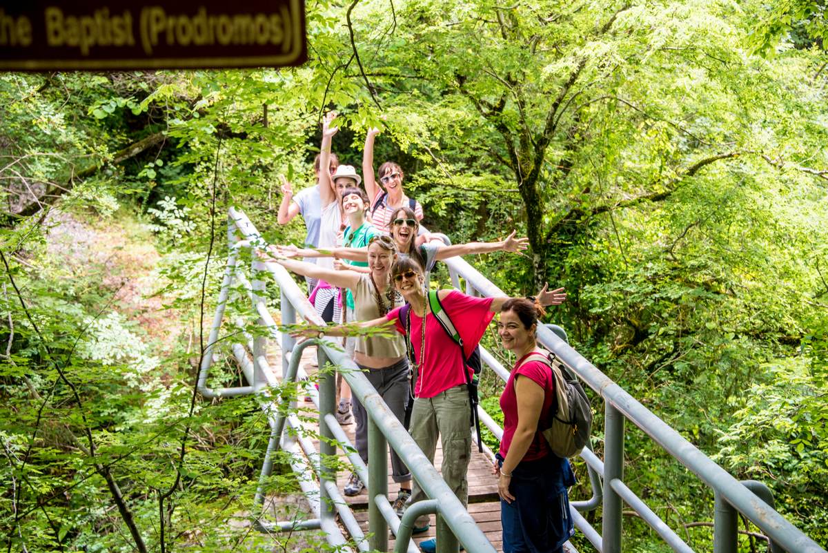 Guided hiking group crossing a stone bridge over the rushing Lousios River in the Menalon mountains