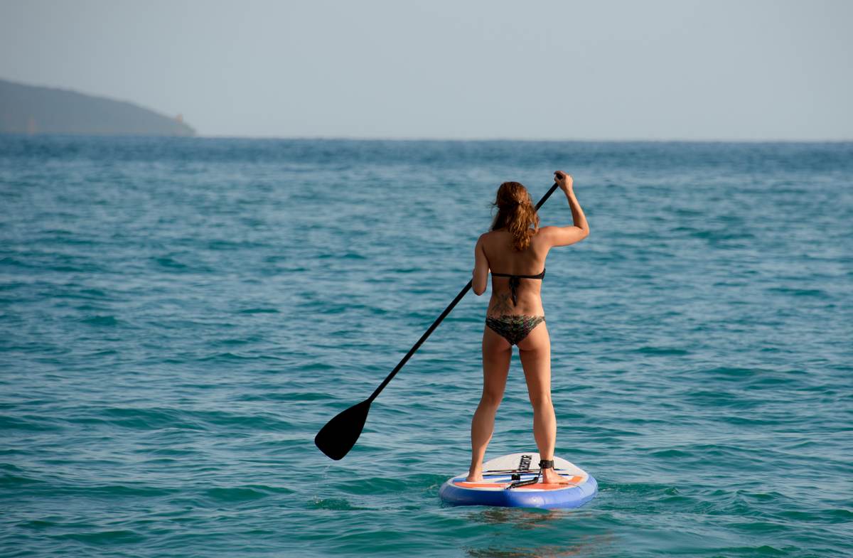 A person paddleboarding on the clear turquoise waters of Voidokilia Bay in Messinia, Greece