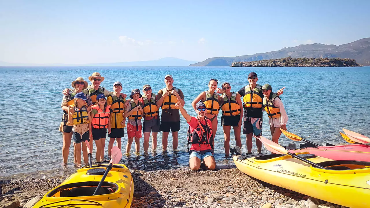 Explore Messinia-Celebrating a fun-filled kayaking adventure. Explore Messinia-A cheerful group posing for a team photo on the beach after a picnic, with their guide and colorful kayaks arranged in the background, celebrating a fun-filled kayaking adventure.