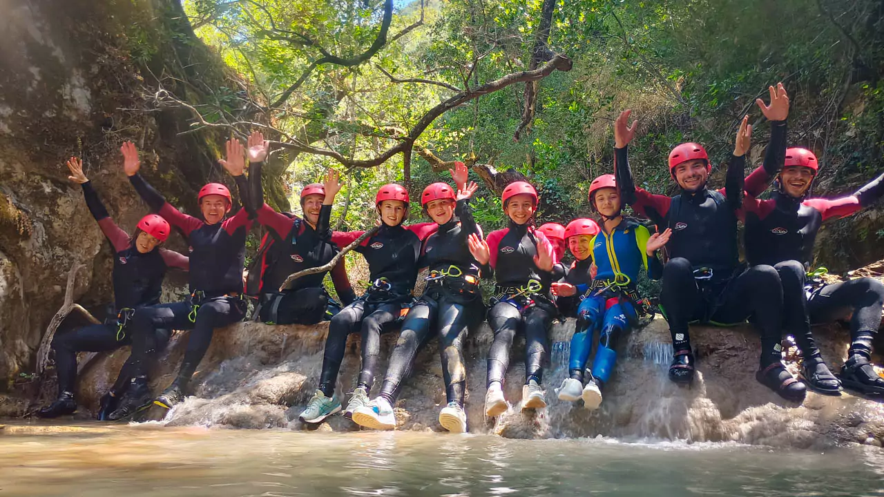 Explore Messinia- Adventurers sliding into a naturally-formed pools surrounded by smooth rocks and dappled sunlight filtering through the trees. Explore Messinia- Adventurers sliding into a naturally-formed pools surrounded by smooth rocks and dappled sunlight filtering through the trees, a highlight of the Neda waterfalls canyoning experience for beginners and families alike.