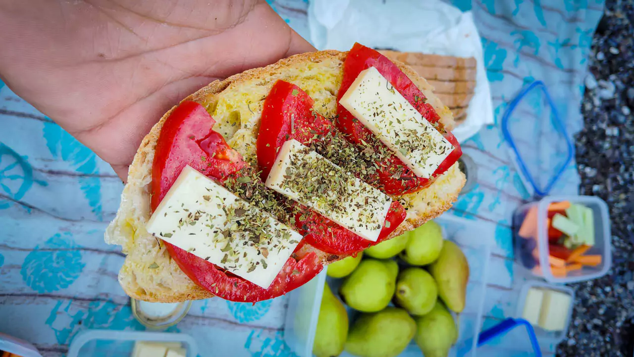 Explore Messinia-A slice of fresh bread topped with juicy tomato slices, graviera cheese, a drizzle of extra virgin olive oil, and a sprinkle of oregano, capturing the essence of a traditional Greek delicacy. Explore Messinia-A close-up of a slice of fresh bread topped with juicy tomato slices, graviera cheese, a drizzle of extra virgin olive oil, and a sprinkle of oregano, capturing the essence of a traditional Greek delicacy enjoyed during a kayak tour picnic.