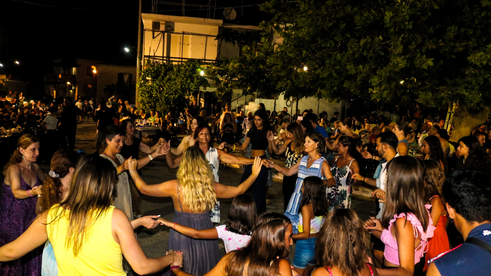 People dancing in a circle at the Okra Festival in Armenioi People dancing in a circle at the Okra Festival in Armenioi, celebrating Messinia’s vibrant traditions and community spirit.